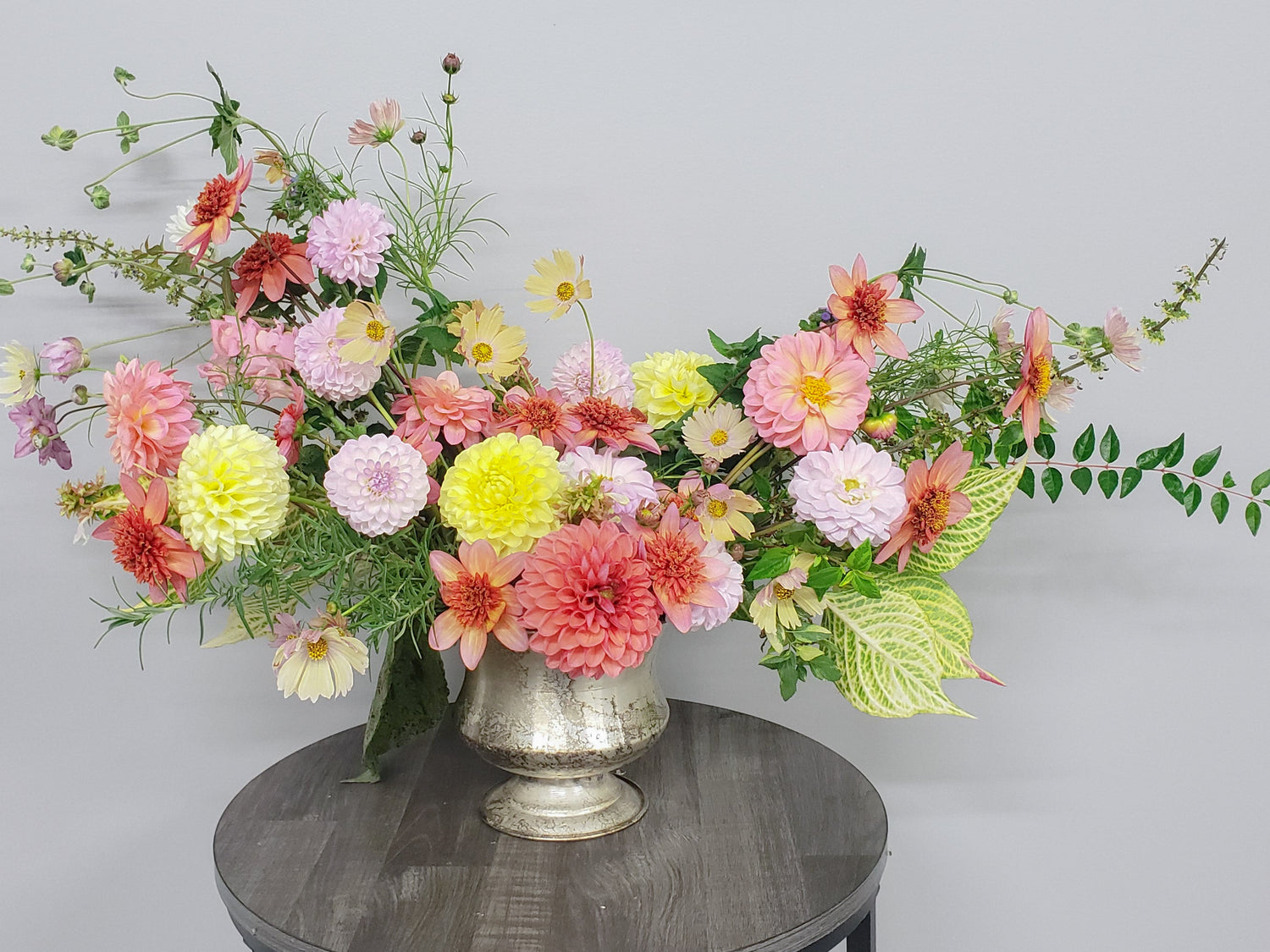 Floral arrangement in a silver vase on a round wooden table against a gray background